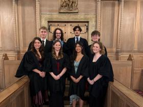 A group of students wearing black academic dress standing in front of some carved wooden doors in the LMH Chapel