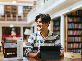 A male student sitting at a desk with a laptop