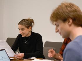 A female student in a tutorial who is looking down at her work and smiling