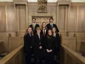 A group of male and female students stand in a group dressed in black academic robes in the LMH chapel