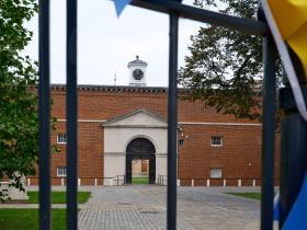 A red brick building seen through some black iron gates covered in bright blue and yellow bunting