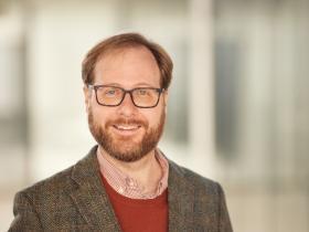 Frank DiTraglia, who has short red-brown hair, a beard and glasses