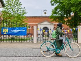 The gates to LMH with a blue banner and a student pushing her bike across the picture