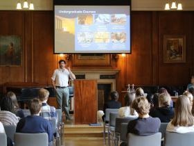 A man stands in the front of a wood-panelled room speaking to a group of students about applying to Oxford