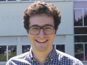 Pablo Bilbao, who has short dark brown hair and glasses, standing in front of a building with lots of windows