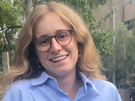 Ariadne Pagoni, who has long light brown hair and is wearing dark framed glasses, smiles at the camera