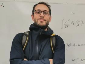 Andrea Medraglia standing in front of a whiteboard with mathematical problems