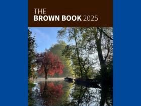 Cover of the Brown Book 2025. Brown background with white text featuring a photo of autumnal trees reflected on water