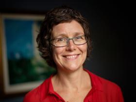 Jo Begbie, who has short dark brown hair and glasses and is wearing a red top