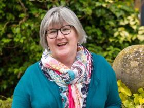 Dr Anne Mullen, who has grey hair tied back in a ponytail, dark rimmed glasses and is wearing a turquoise top and colourful scarf