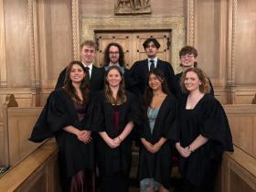 A group of smiling students wearing black academic gowns standing in the LMH Chapel