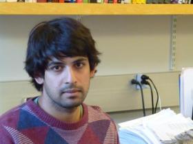 Varun Kanade, who is wearing a jumper in different shades of purple and has dark hair, sitting in an office