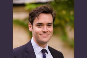 Joshua Bennet, who has short dark brown hair, wearing a dark suit and tie