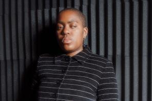 Onyeka Igwe, dressed in a black blazer and leaning against a black wall