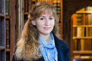 Cosima Gillhammer, a woman with long wavy blonde hair, stands in a library