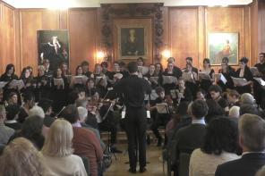 A choir dressed all in black performing in a wood-panelled room
