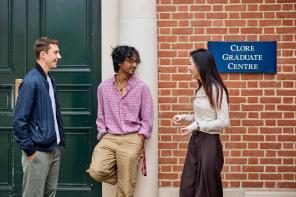 Two male and one female student lean against a red brick building, the Clore Graduate Centre