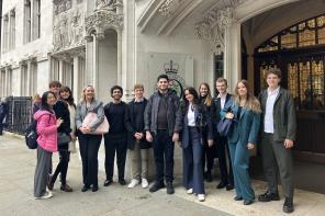 A group of 10-15 students stand smiling at the doors of a grand-looking white stone building in London