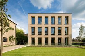 A modern sandstone building standing in front of a green quad of grass