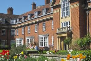 A red brick building with many windows, and in the foreground bright coloured tulips flower in a garden
