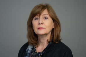Portrait of Professor Christine Gerrard, wearing a dark sweater and patterned scarf, against a plain grey background