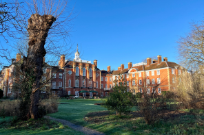 The gardens of Lady Margaret Hall in the winter. A red brick building with a bright blue sky in the background