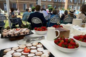 Guests strolling through the LMH gardens in bright summer sunshine during the 2025 Alumni Garden Party, with families and alumni gathered near the red-brick building.