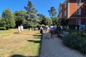 Guests strolling through the LMH gardens in bright summer sunshine during the 2025 Alumni Garden Party, with families and alumni gathered near the red-brick building.