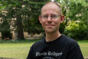 Peter Thonemann, who has very short brown hair, rimless glasses and is wearing a black t-shirt with 'Phoebe Bridgers' printed on it