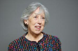 Baroness Manningham-Buller, an older woman with grey hair, wearing a colourful textured jacket, smiling against a plain grey background