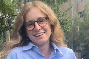 Ariadne Pagoni, who has long light brown hair and is wearing dark framed glasses, smiles at the camera