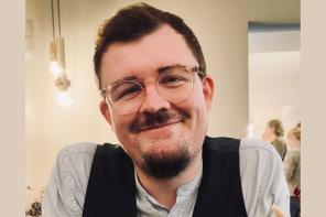 Florian Lutzelberger, who has short dark hair and a dark beard and moustache and clear-framed glasses is smiling at the camera