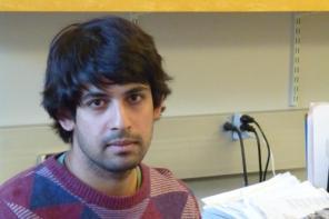 Varun Kanade, who is wearing a jumper in different shades of purple and has dark hair, sitting in an office