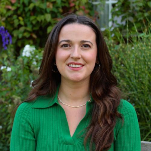 Ava Harrison, who has long dark brown hair, sitting on a bench surrounded by gardens