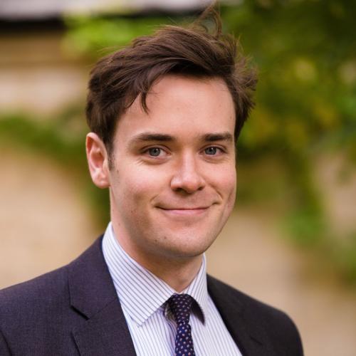 Joshua Bennet, who has short dark brown hair, wearing a dark suit and tie