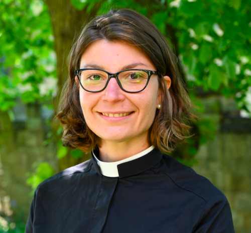 Stephanie Burette, who has shoulder-length brown hair, glasses and is wearing clerical dress