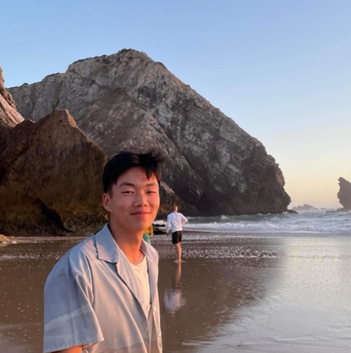 A man with short dark hair stands on a beach