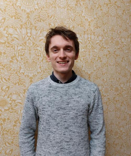 Tom against yellow wallpaper, smiling at the camera