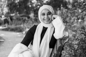 Black and white photo of Sharifah Alihinai sitting on a bench under a tree