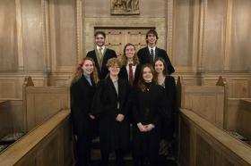 A group of male and female students stand in a group dressed in black academic robes in the LMH chapel