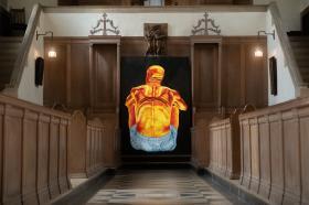 Grace Steinbergs painting of a mans back in vivid orange colouring, wearing blue shorts on a black background