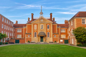 A grand Edwardian building overlooks a quad with a large green lawn.