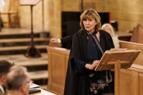 Professor Christine Gerrard, wearing black academic robes, standing at a wooden lectern in the LMH Chapel