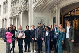 A group of 10-15 students stand smiling at the doors of a grand-looking white stone building in London