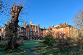 The gardens of Lady Margaret Hall in the winter. A red brick building with a bright blue sky in the background