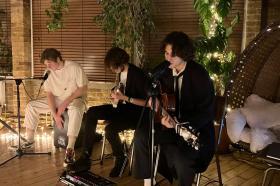 The band Mount St. Helen, comprising two young men playing guitar and one playing a drum with his hands, performing in an intimate gig session