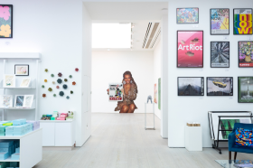 A shot of a white-walled gallery with brightly coloured artworks displayed on the walls. 
