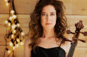 Close-up picture of Elinor Frey, who has long curly brown hair and is wearing a black dress and holding a Cello