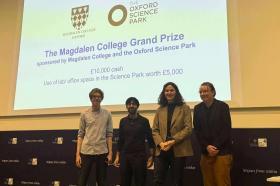 Four students stand on a stage in front of a screen saying: The Magdalen College Grand Prize