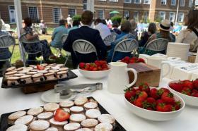 Guests strolling through the LMH gardens in bright summer sunshine during the 2025 Alumni Garden Party, with families and alumni gathered near the red-brick building.
